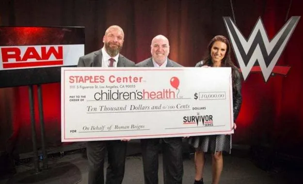 El Staples Center dona 10,000$ en nombre de Roman Reigns, Triple H y Stephanie McMahon reciben el cheque.